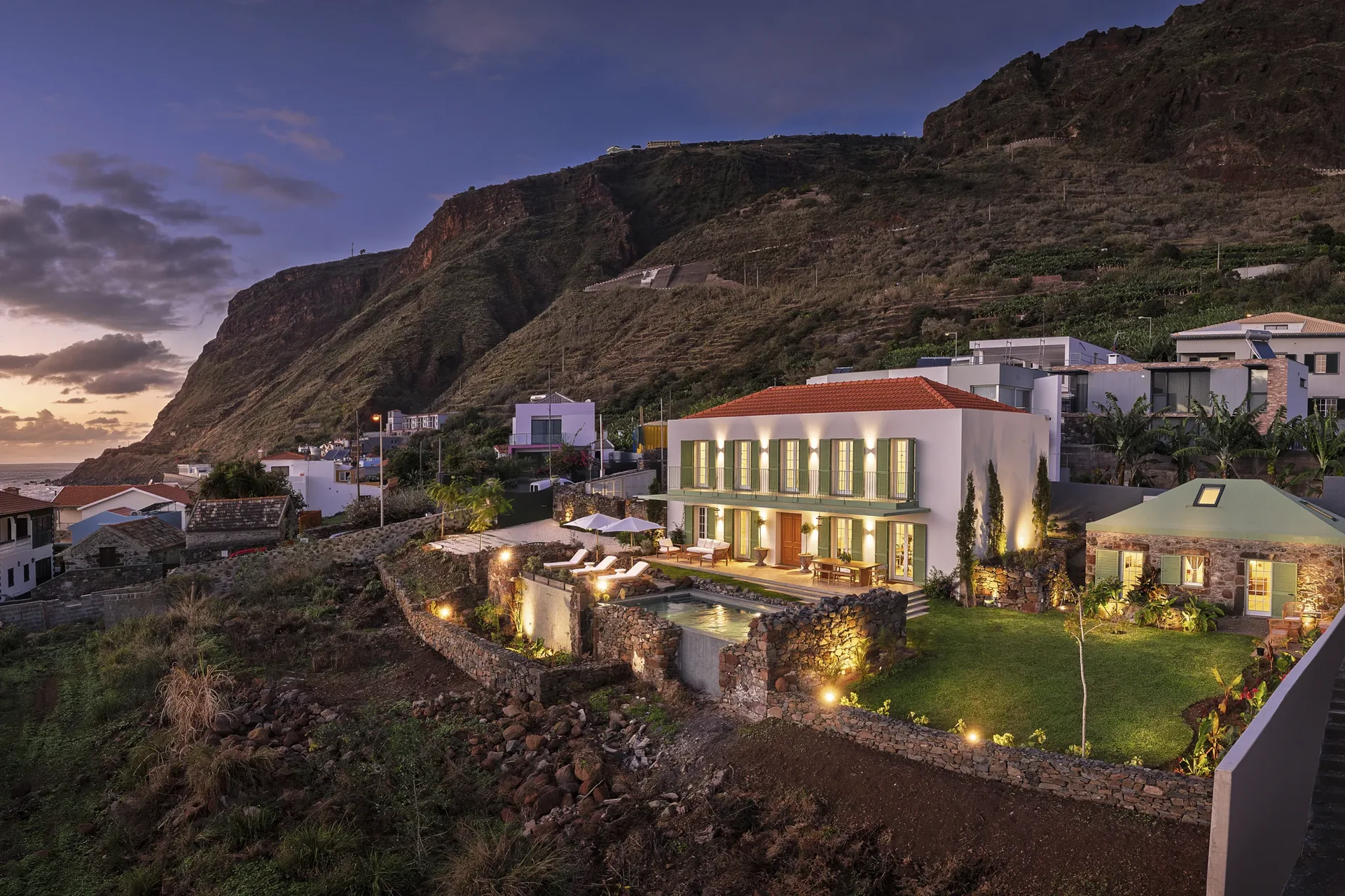 A Casa no Paul do Mar iluminada ao anoitecer, sob a falésia da Calheta.