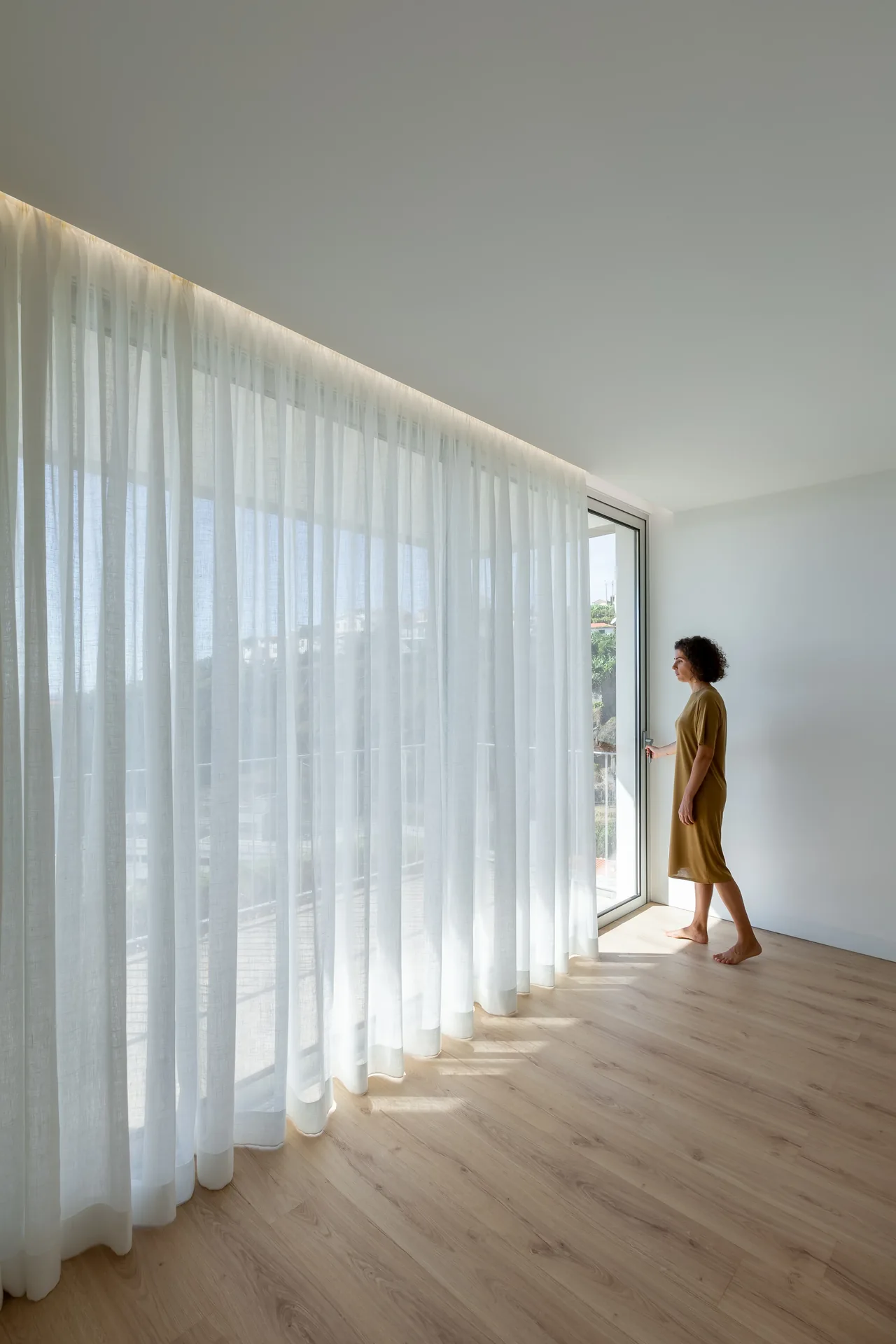 Sala com cortinado leve ao longo da fachada sul, na Casa no Serrado da Adega.
